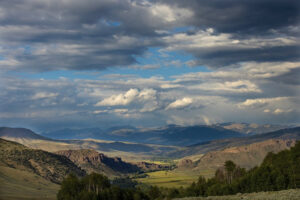 A green valley with dancing moody clouds sitting on top of the mountains on a day that threatens rain.