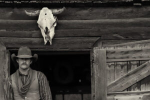 A stoney-faced young cowboy below a mounted steer head skull.