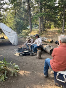 A couple of ranchers cooking breakfast over an open flame on the trail at Shoshone Lodge while the photographer captures the scene.
